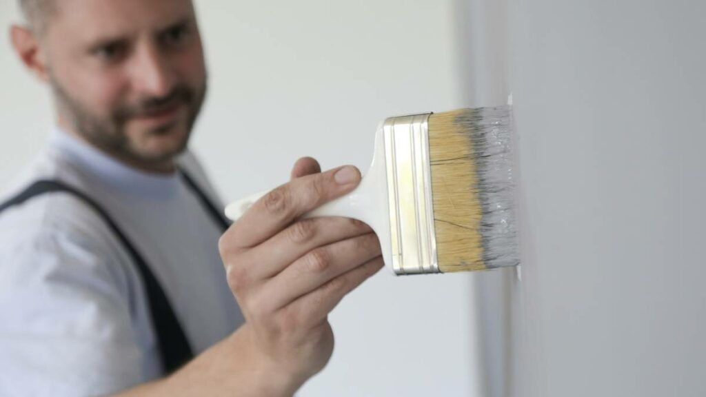a man painting an interior wall using a paintbrush