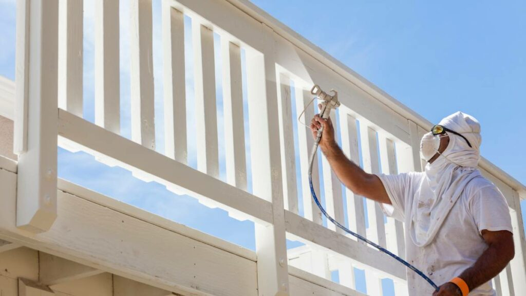 a painting contractor spray painting the deck of a house