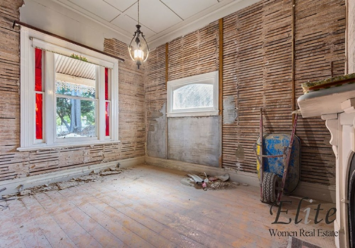 Room undergoing renovation with dusty wooden floors and guttered walls.