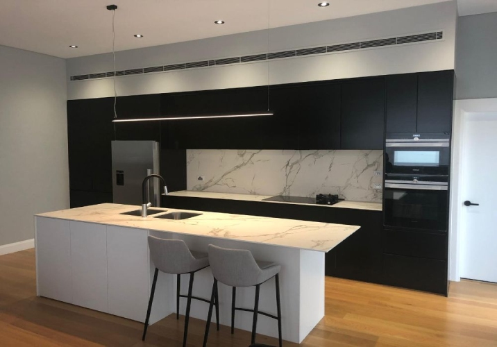 Modern kitchen with black cabinetry, marble island benchtop and splashback. 