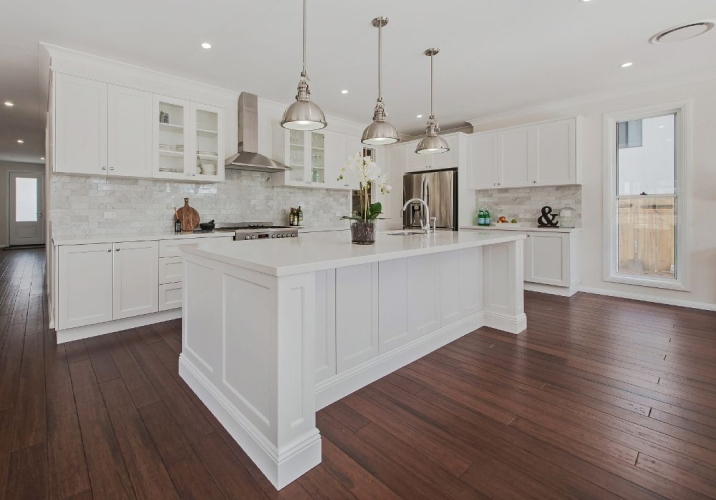 Brown hardwood flooring in a bright kitchen with white cabinetry and island bench. 