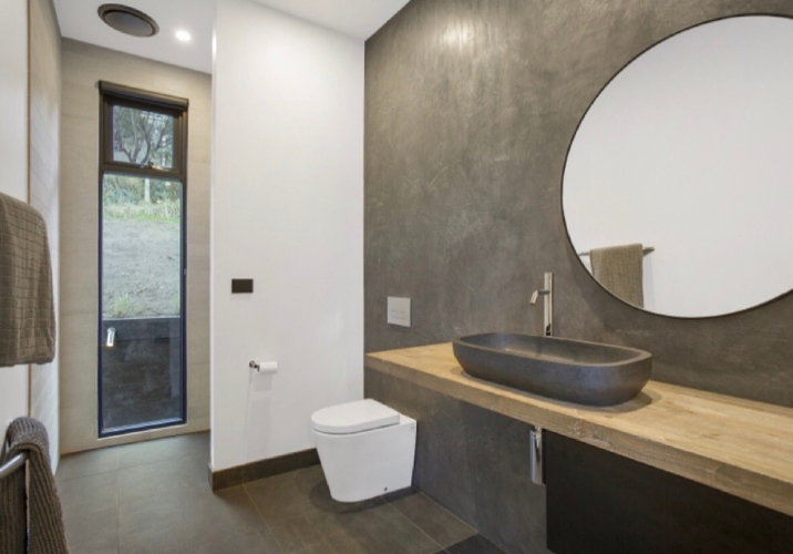 Large neutral coloured bathroom with round mirror sink and wall mounted toilet