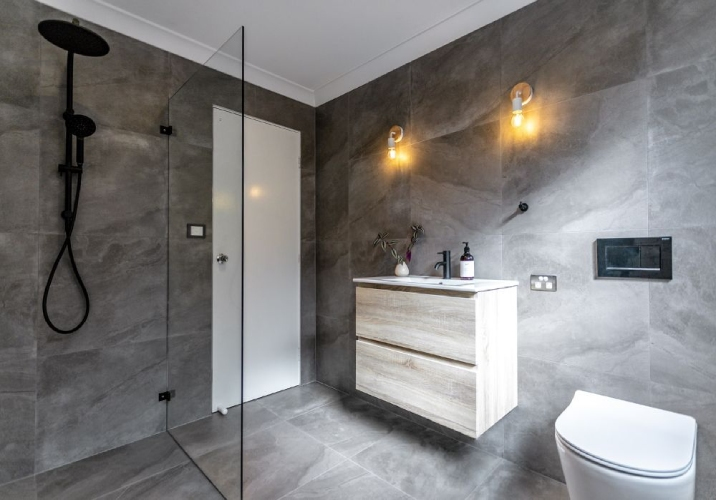 Modern dark tiled bathroom with dark fittings.