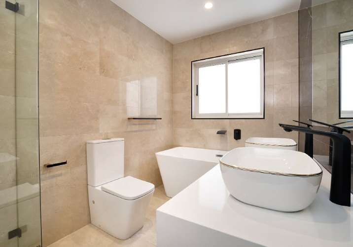 Light brown tiled bathroom with double vanity, stand alone bathtub and toilet.
