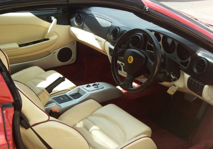 Interior of a red ferrari with white leather seats and black steering wheel.