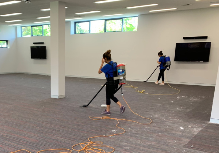 Two women vacuuming debris on a carpet 