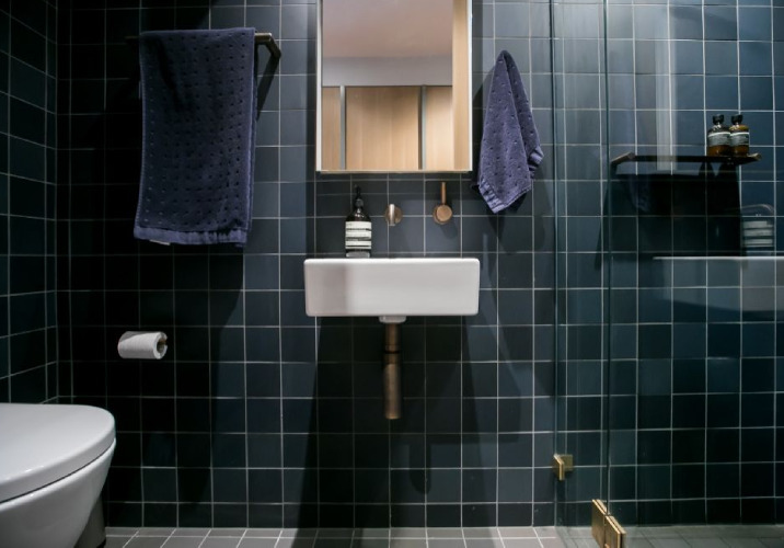 A dark blue bath towel and hand towel in a bathroom with dark tiles