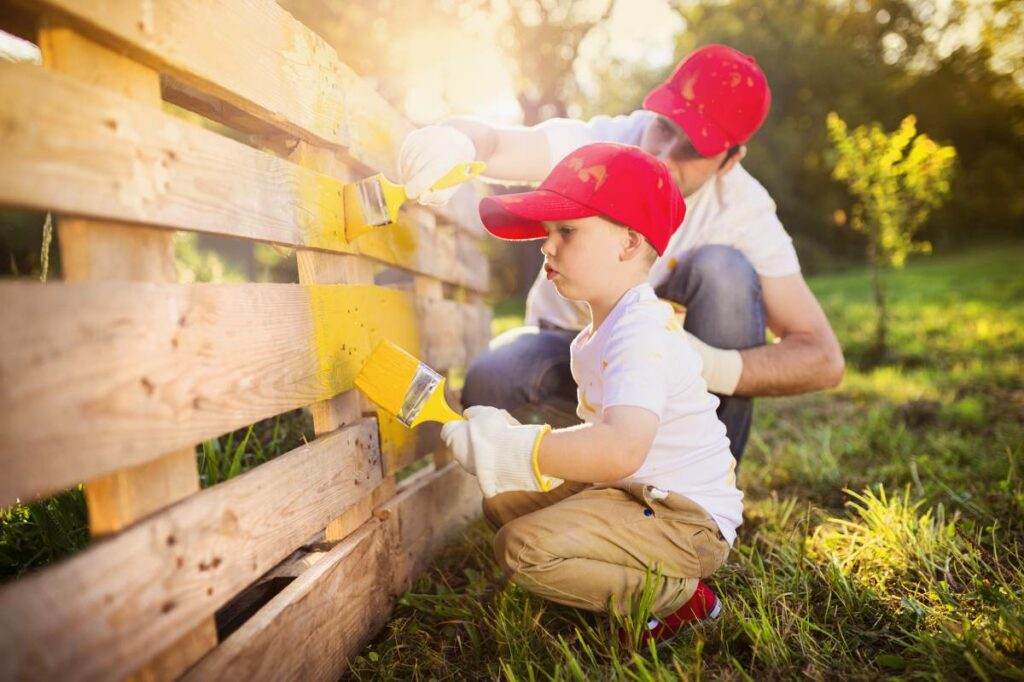 A little boy and his dad painting their yard fence together