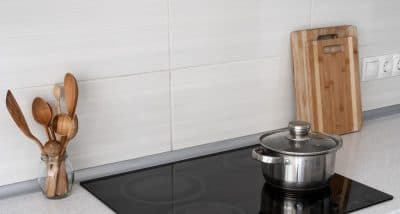 Black cooktop on a white quartz benchtop with pot, 2 wooden chopping boards and wooden spoon.