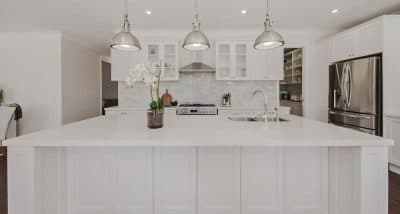All white kitchen with stainless steel appliances, tile splashback and three pendant lights.