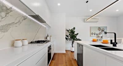 White kitchen, timber floorboards, marble splashback with black furnishes and steel appliances.