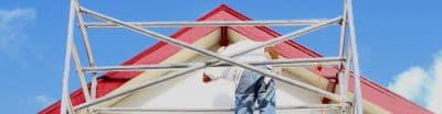 Man standing on scaffolding painting a house