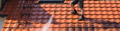 Man on a roof using a high pressure hose