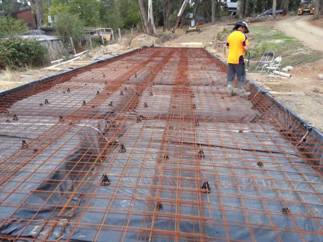 Steel reinforcing mesh and bars for large driveway are inspected by professional wearing hard hat and hi vis shirt.