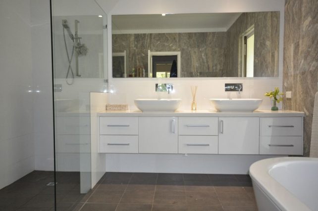 Modern bathroom with dark floor tiles, marble wall tiles and two white basins.