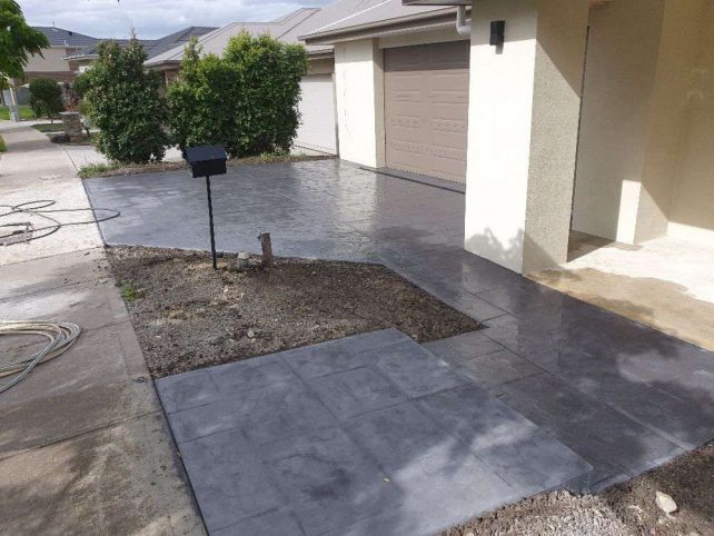 Recently completed dark grey patterned driveway connects to rendered white house.