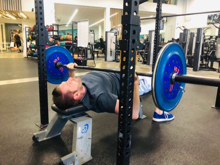 Man laying on bench pushing up barbell up towards the ceiling.