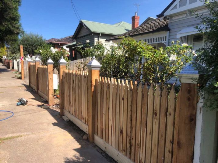 Wooden picket fence in front of a white cottage house and garden.