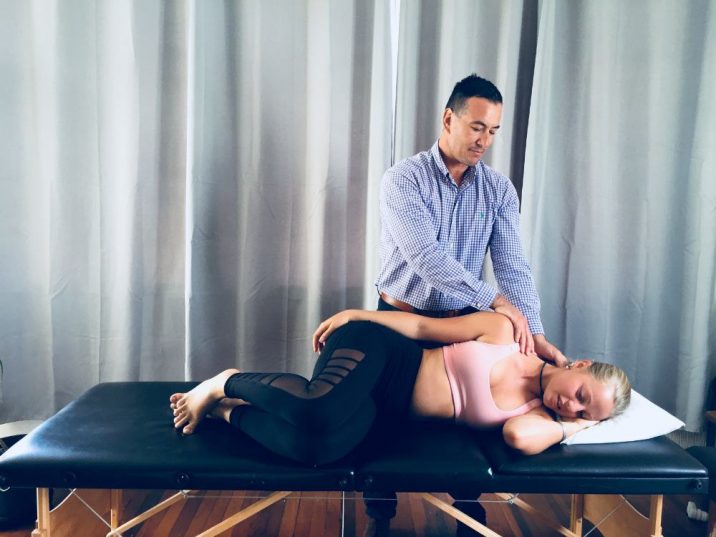 Male masseuse gently massages the neck of a female patient laying on her side.