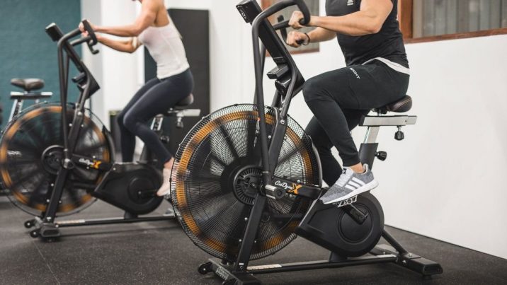 Two people ride stationary air bikes indoors.