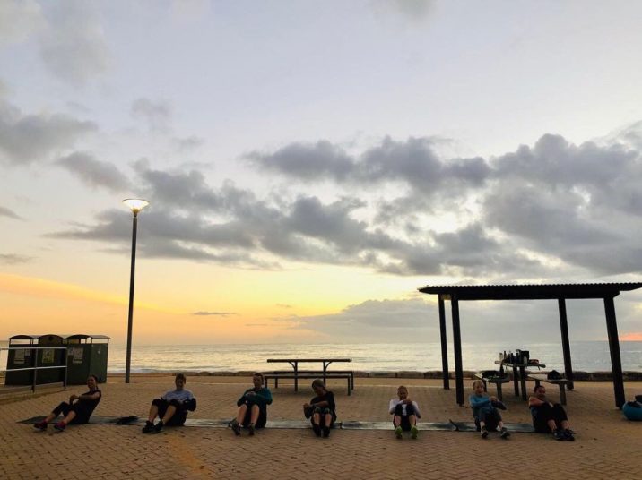 Group of women participating in core exercises by the beach.