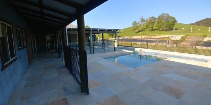 A sandstoned tiled backyard with pool overlooking hill with trees and farm animals.