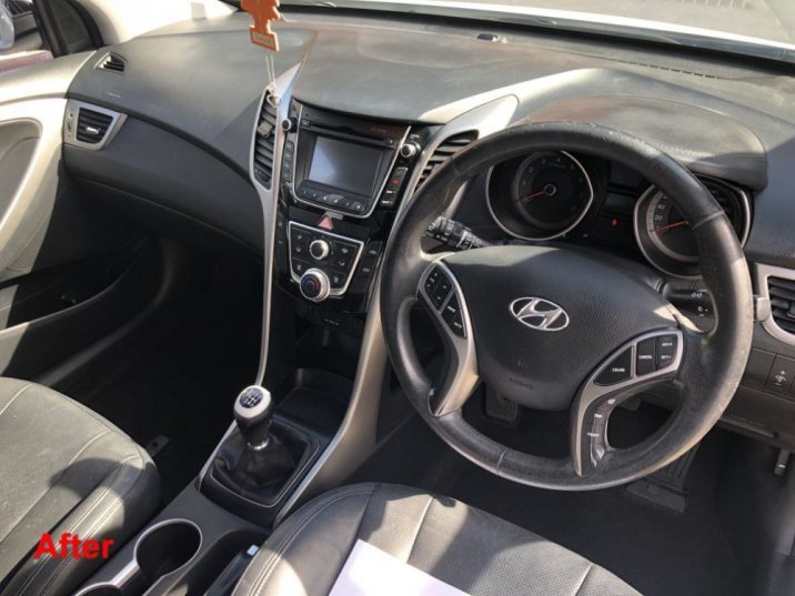 Dark interior of a manual hyundai vehicle showing steering wheel, gear stick and dashboard.