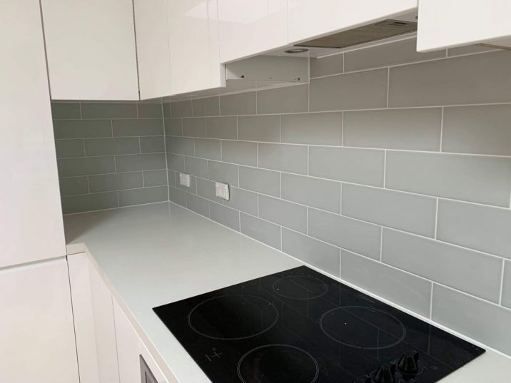 A grey tiled kitchen splashback with black stove on bench.
