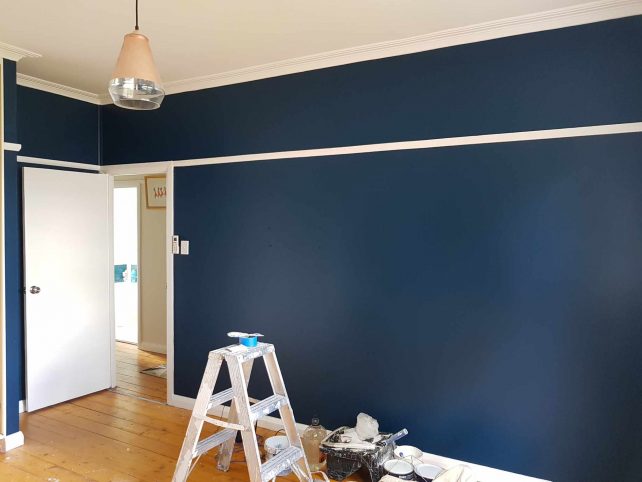 Navy blue wall with white trims, timber flooring and pendant light hanging from the ceiling.