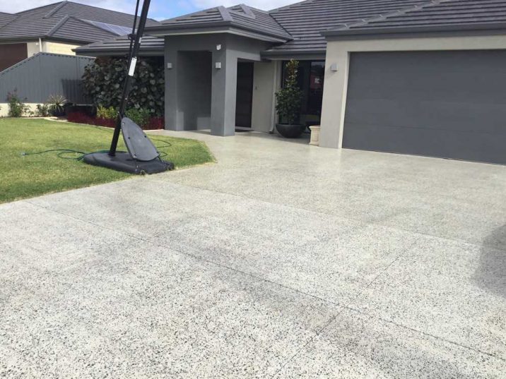 White polished concrete driveway leads to a grey cement rendered house.