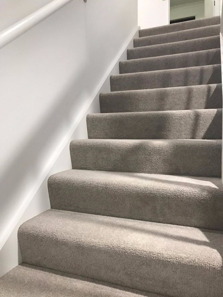 Set of grey carpeted stairs next to white wall with handrail.
