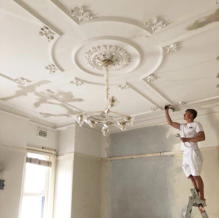 Painter hand painting details onto a ceiling.