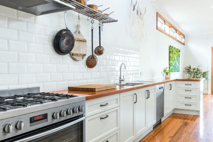 Bright kitchen with white tile splashback, timber bench and stainless steel appliances.
