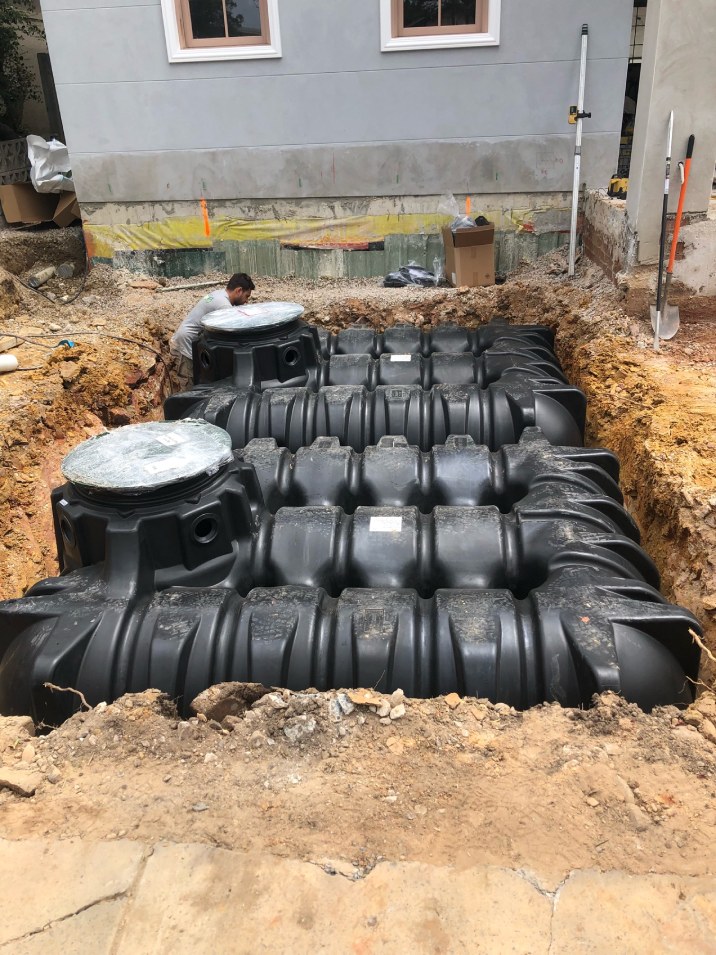 Black septic tank being constructed in the ground of a backyard home.