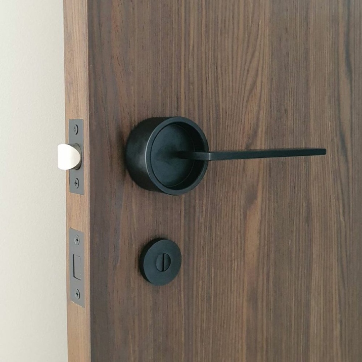 An ajar brown timber door with a sleek black handle and lock