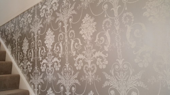 Bronze and white patterned wallpaper next to a set of carpeted stairs.