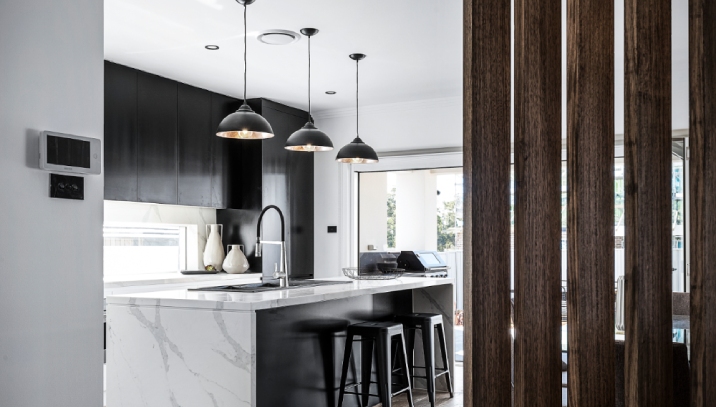 Modern kitchen with black cabinets, marble benchtop and three pendant lights hanging over the sink.