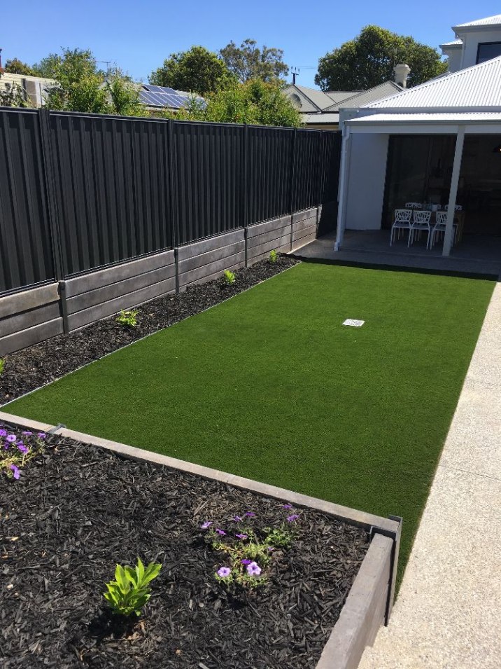 Small strip of green artificial turf surrounded by garden beds in a backyard.
