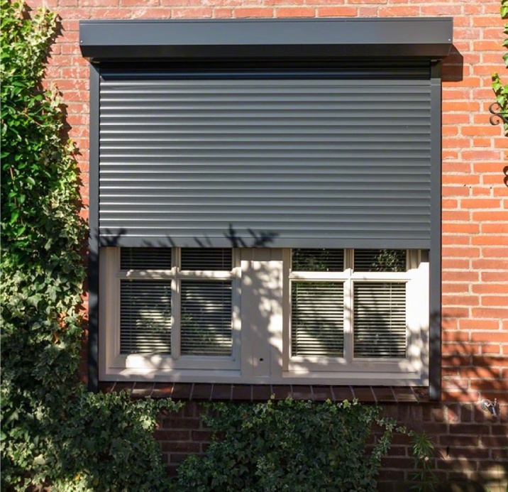 A half opened black outdoor security shutter on a red brick house.