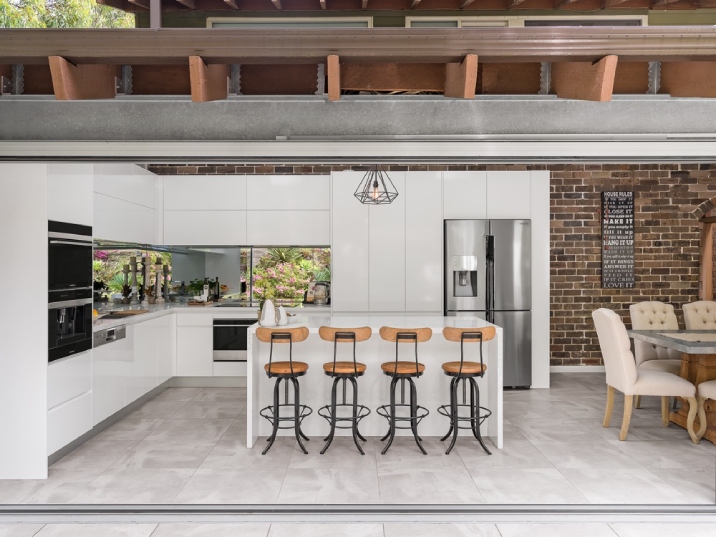 Bright indoor-outdoor kitchen with white cabinets, bench and timber seats.