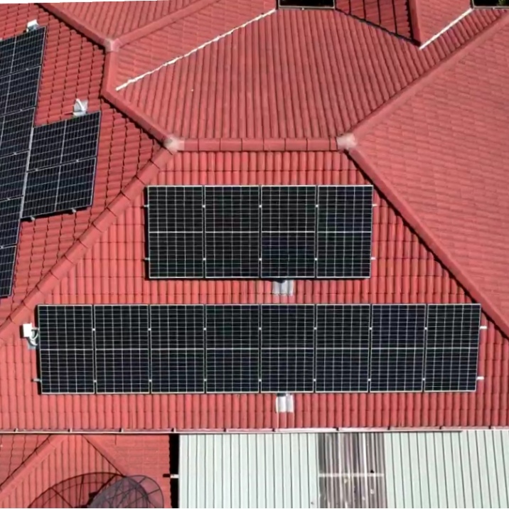 Aerial view of a red tiled house with solar panels on two sides of it.