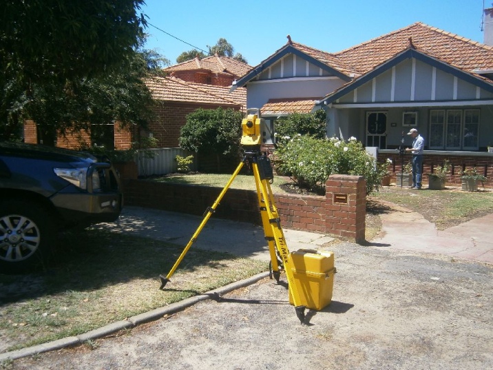 Surveyor has tripod equipment set up in the front yard of a house. 