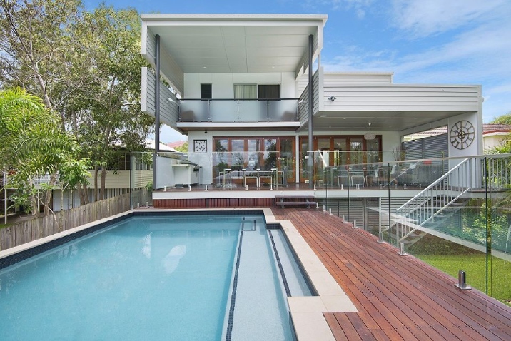 A rectangular concrete pool with a deck leading of from a two-storey house.