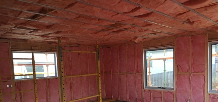 A room being constructed is lined with pink insulation on the walls and ceiling.