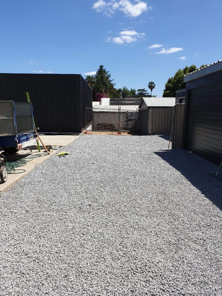 Blue gravel leading to a garage with the rear end of a ute on the other side.