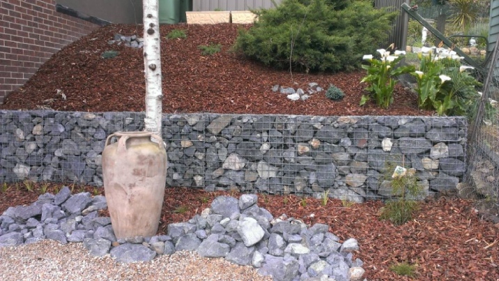 A gabion retaining wall separates a mulched garden from the one below.