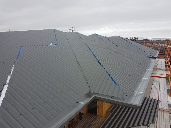 Dark grey tin roof with grey gutters on a constructed house.
