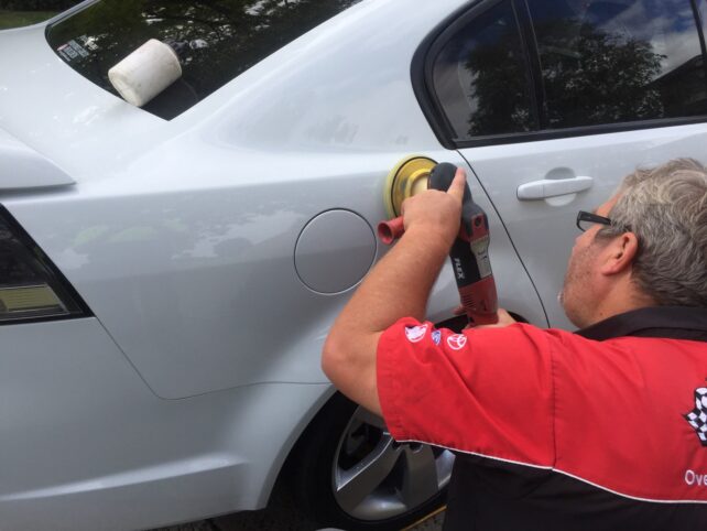 Man using polishing tool to buff marks out of a white car
