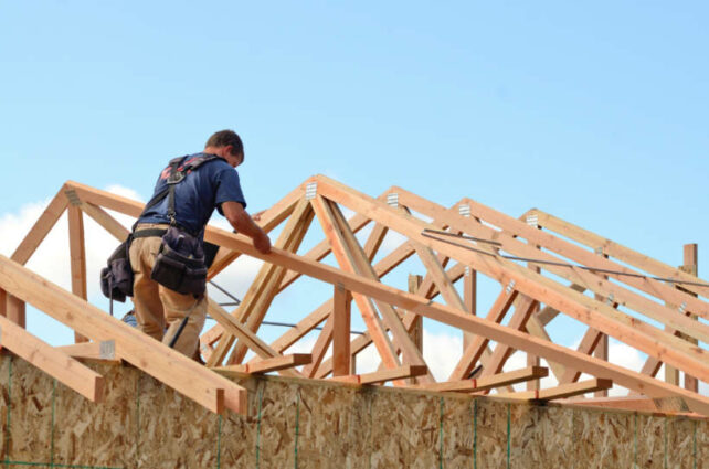 Australian building standards - Construction worker assembling a wooden roof frame on a building site.