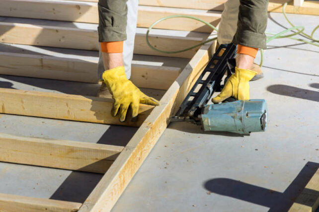 Australian framing standards - Close-up of a construction worker using a nail gun to secure wooden beams.